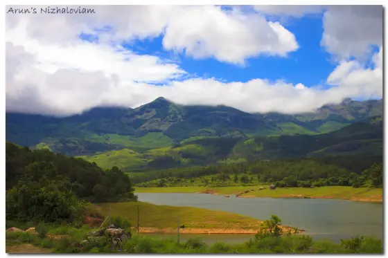 Blue water and grassy shores at Anayirankal beneath a broad, bright sky.