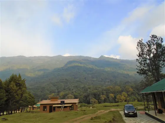 Low ochre buildings and a parked car at Pampadum Shola’s nature-education centre below the forested hillside.