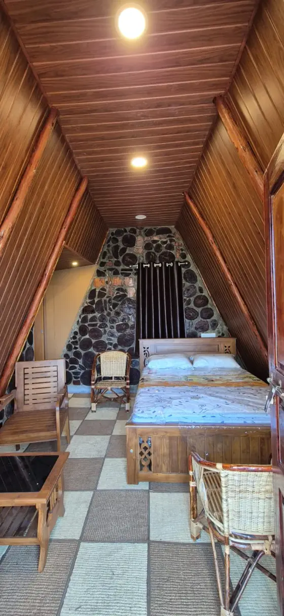A bed and chairs under the timber ceiling of Chundal A Frame Log House.