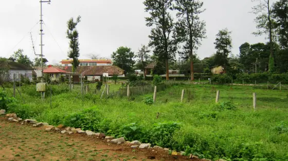 The working end of the farm: sheds and offices behind a wire fence, an aerial mast, and rough ground waiting to be turned over.