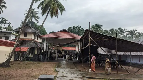 The courtyard on a wet morning: the tiled ranges of the temple with a temporary shelter rigged over the forecourt and worshippers crossing between them.