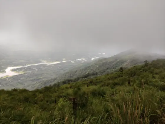 A pale bend of water appears beyond Ilaveezhapoonchira’s grassy slope under a low layer of cloud.