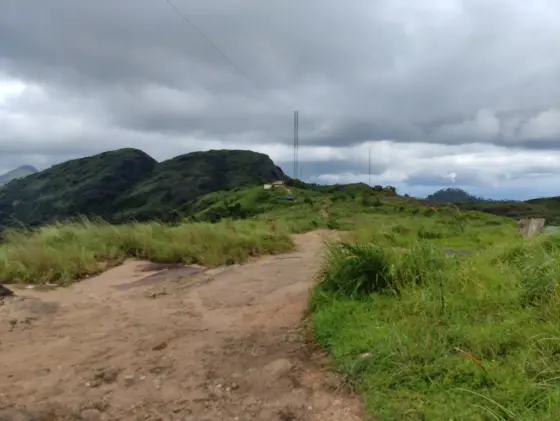 A broad earth-and-rock track crosses grass towards masts and rounded hills at Ilaveezhapoonchira.