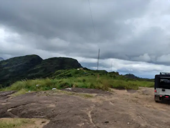 A jeep stands on an earth-and-rock approach beside grass and slender masts beneath dark cloud at Ilaveezhapoonchira.