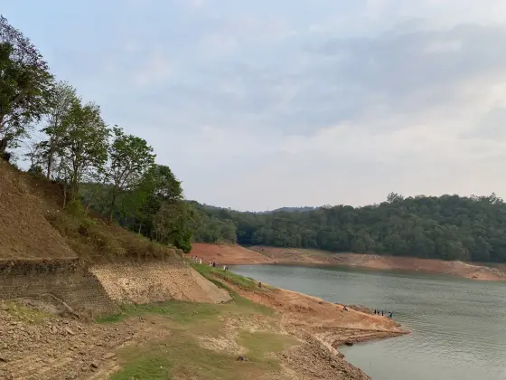Reddish exposed banks curve around Ponmudi reservoir below wooded slopes.