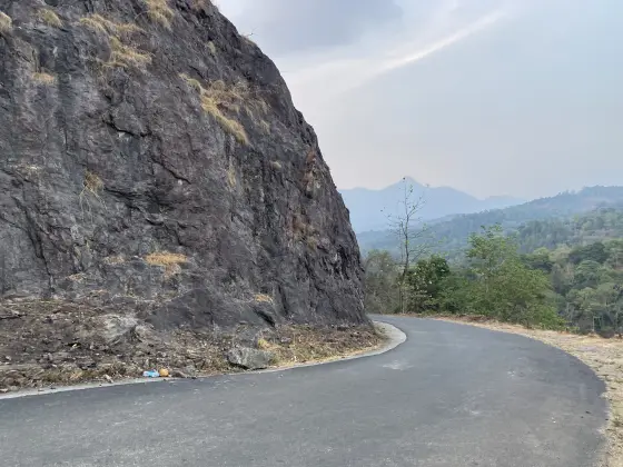 The approach road curves beneath a large exposed rock face near Ponmudi Dam.
