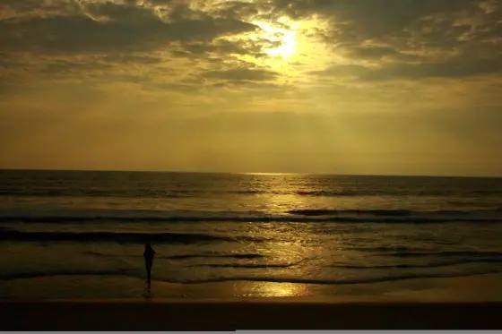 A visitor stands on Valiyaparamba’s Arabian Sea beach beneath a golden evening sky; this is the sea-facing shore, not the backwater.
