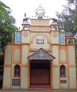 The ochre St Thomas Ecumenical Church entrance, with a cross above the doorway and devotional symbols across the facade.