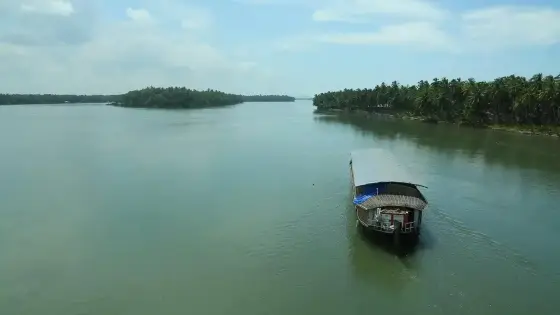 A roofed boat approaches through a broad channel between coconut-lined islands.