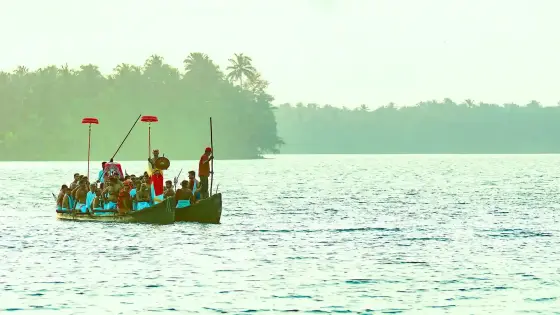 A ceremonial canoe carries participants, poles and red parasols across Valiyaparamba Backwaters.