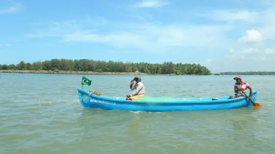 Two men travel in a narrow blue canoe on Valiyaparamba’s water.