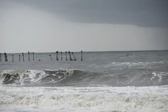 Rough grey waves break beside the old pier-post remains.