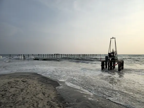A line of pier posts extends through the surf, with a separate piled platform in the foreground.