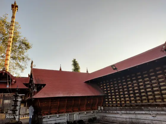 A tall golden flagstaff stands beside a red sloping roof and a wall lined with lamps.