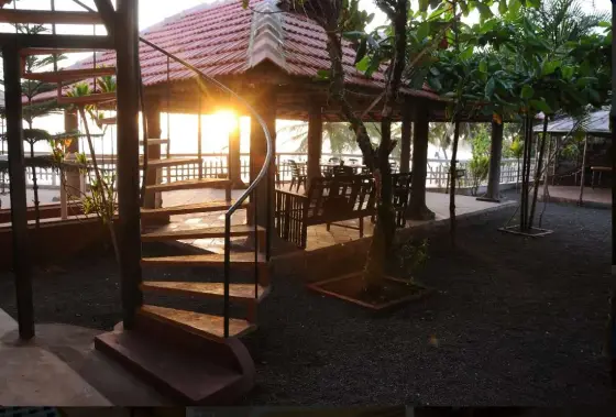 Evening light through a tiled pavilion at Seashell Haris Beach Home in Adikadalayi, with a spiral stair and wooden seating; private accommodation context.