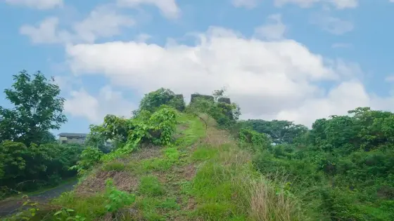 A grass-covered ramp rises towards Hosdurg’s ruined bastion beneath a blue, clouded sky.