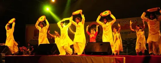 Performers in yellow costumes lift round props on a lit stage in an archival Nattika Beach Festival photograph.