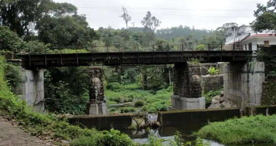 An older metal-beam bridge on masonry piers beside a newer crossing in Peermade.