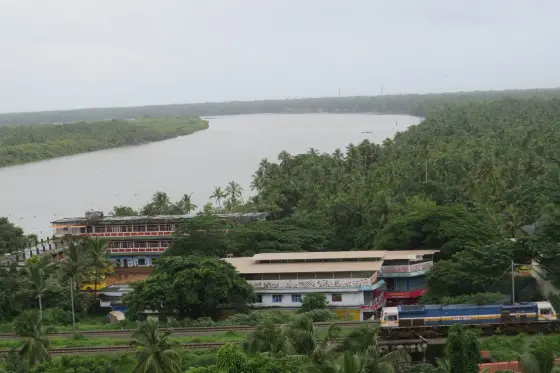 A train and railway line below Madayipara, beyond the water and coconut-covered settlement.