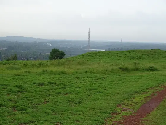 The settled lowland beyond Madayipara’s grassy edge, with telecommunications towers in the view.