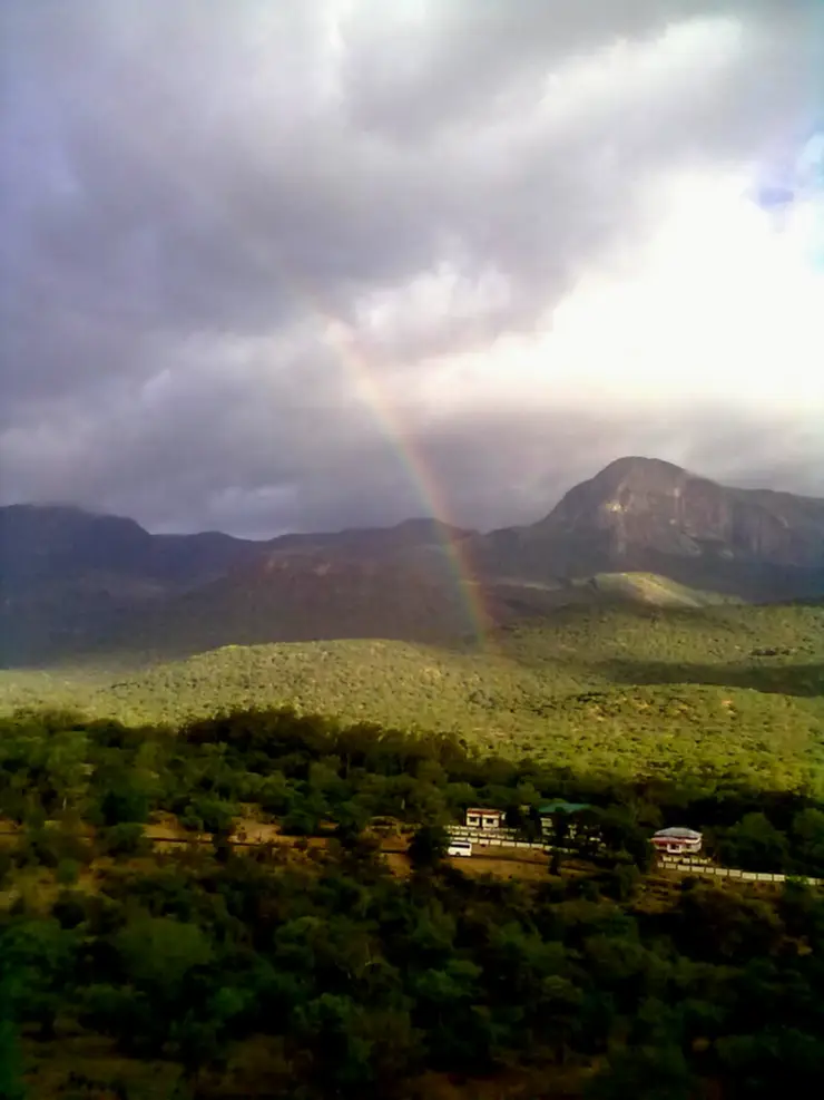 A rainbow arcing over a wide valley of dry green hills in Chinnar Wildlife Sanctuary, seen from the watch tower