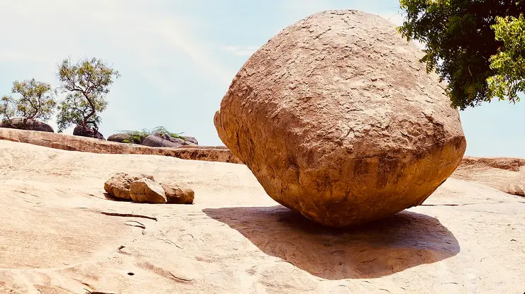 A huge rounded granite boulder resting on a bare rock slope at Mamallapuram, appearing to balance impossibly