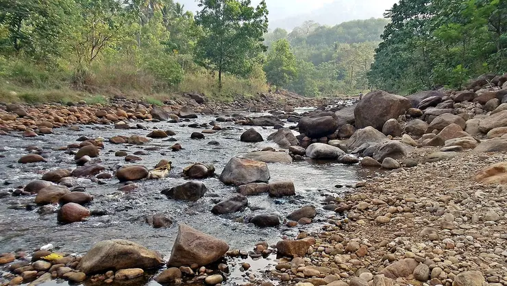 The Kallar river running over a bed of rounded boulders and golden-brown pebbles below forested hills