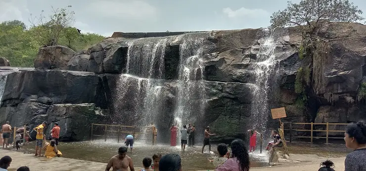 Broad, low sheet of water spilling over a rock ledge at Thirparappu Falls in the monsoon.