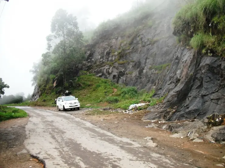 A wet narrow road between a rock-cut bank and vegetation on the Pothamedu approach, in an older photograph.