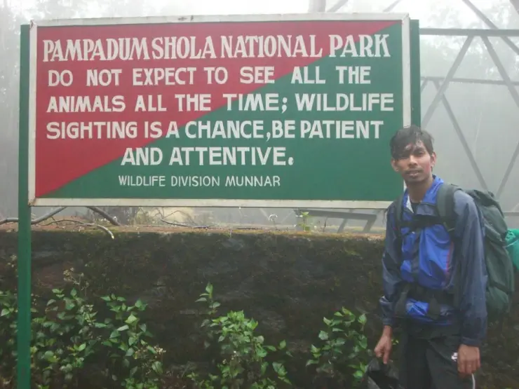 A visitor stands beside a forest sign in the Pampadum Shola landscape.