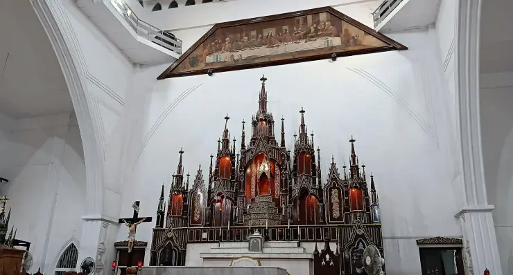 The dark timber Gothic reredos of Mount Carmel Cathedral against a white apse, with a large framed Last Supper painting hung above