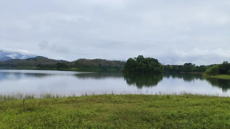 The Peruvannamuzhi reservoir under monsoon cloud, a wooded island at its centre and the Western Ghats receding behind.