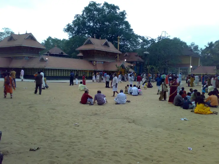 The tiled gabled roofs of the Sarkaradevi Temple at Chirayinkeezhu above its broad sand courtyard, with devotees seated
