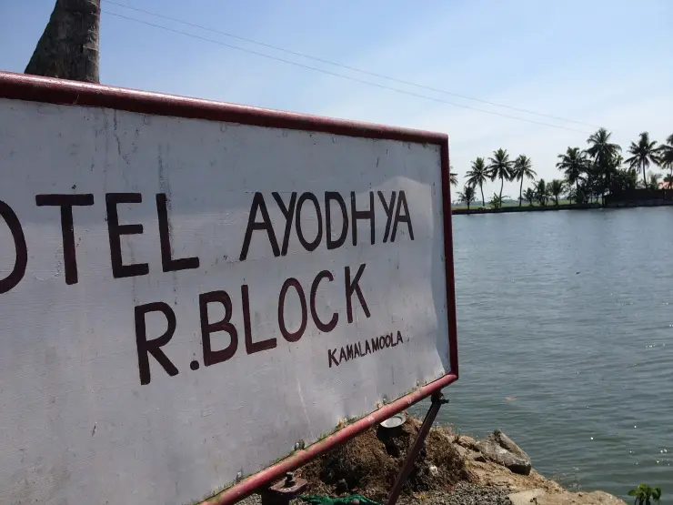 A hand-painted signboard reading Hotel Ayodhya, R.Block, Kamalamoola, beside the open water of Vembanad Lake