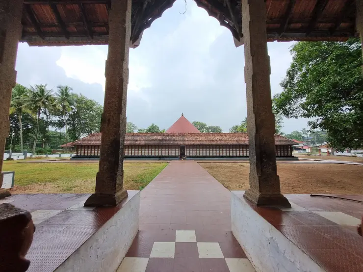 The conical roof of the circular sanctum at Thrikkakara Vamana Temple, seen between granite pillars across the temple courtyard
