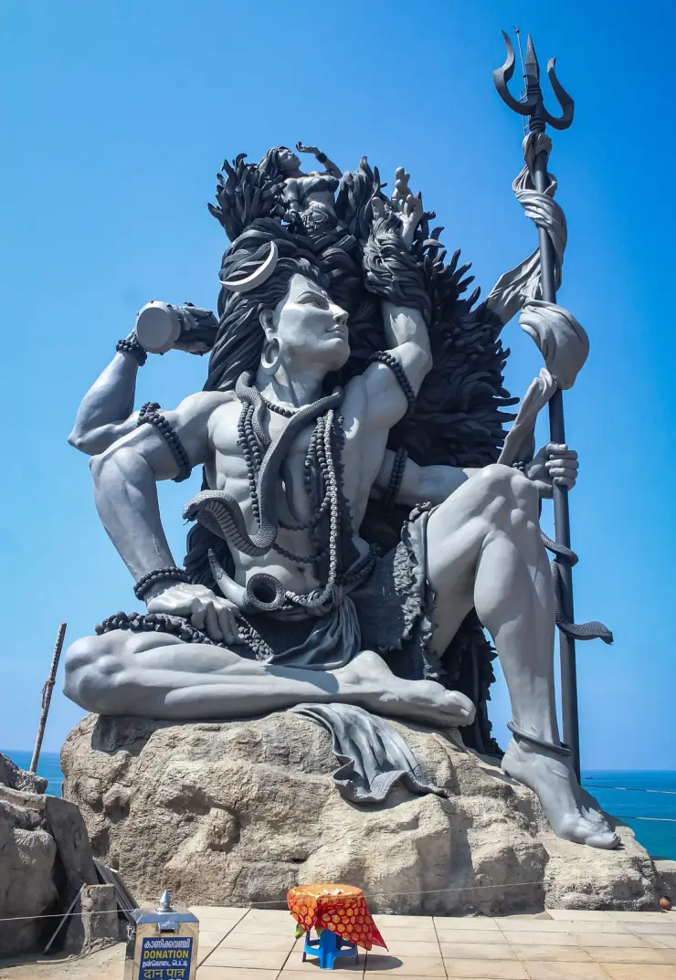The full Gangadhareswara sculpture at Aazhimala seated on its rock above the Arabian Sea, trishul raised, with the sea horizon behind