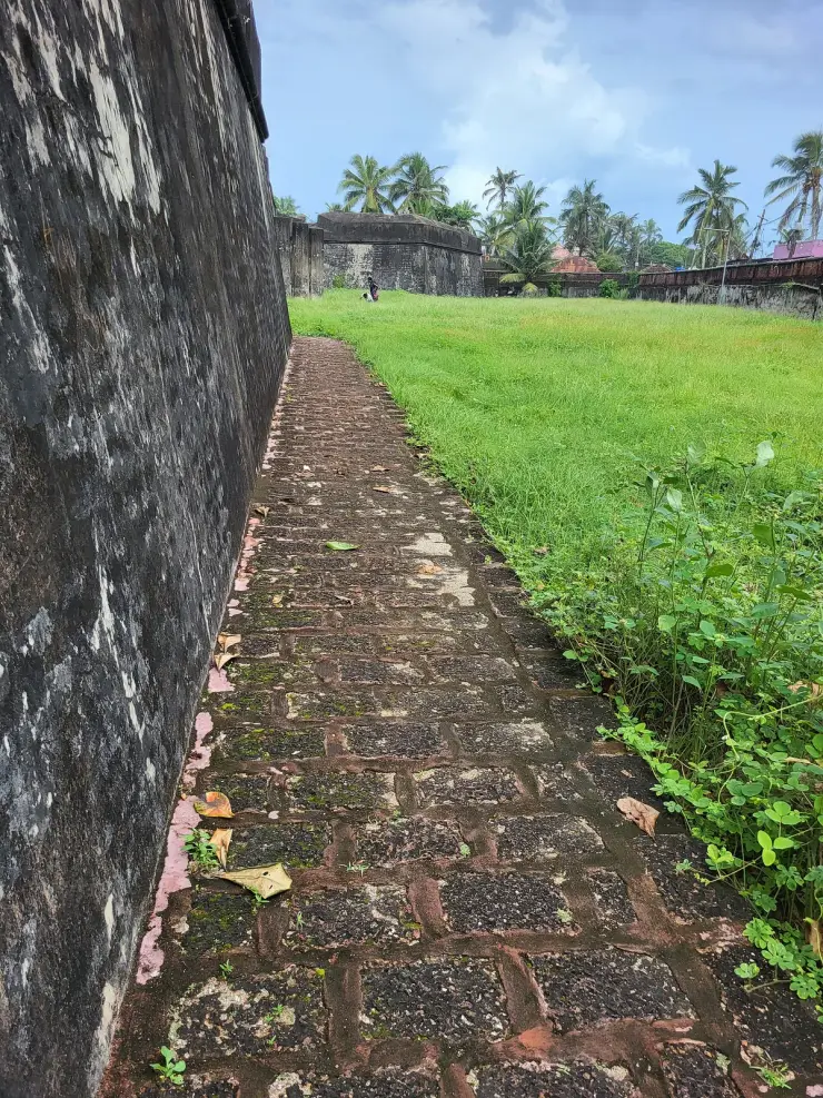 A brick path running along the inside of the laterite rampart at Anchuthengu Fort, with the bastion and green interior beyond