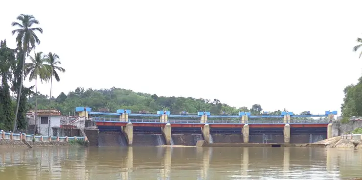 The full width of Aruvikkara Dam across the Karamana river, a low gated masonry wall with the temple buildings at one end