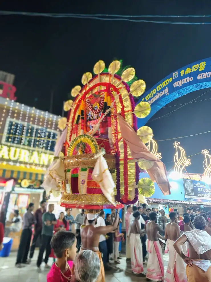 A decorated ceremonial offering carried on the head amid drummers in traditional mundu at the Attukal Bhagavathy Temple festival at night