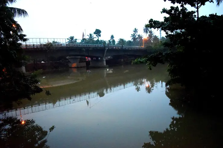 The Karamana river at dusk near the Thiruvallam Parasurama temple, with a road bridge crossing and palms reflected in still water