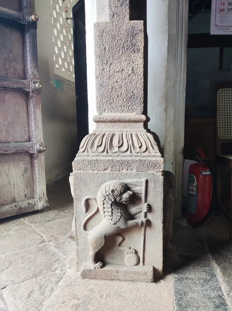 A carved granite pillar base in the Napier Museum showing a rampant lion holding a staff, with an old panelled wooden door behind