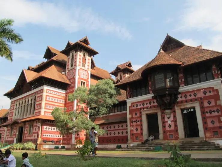 The polychrome exterior of the Napier Museum with its gabled tiled roofs and red, black and cream banding, seen across the lawns of the museum complex