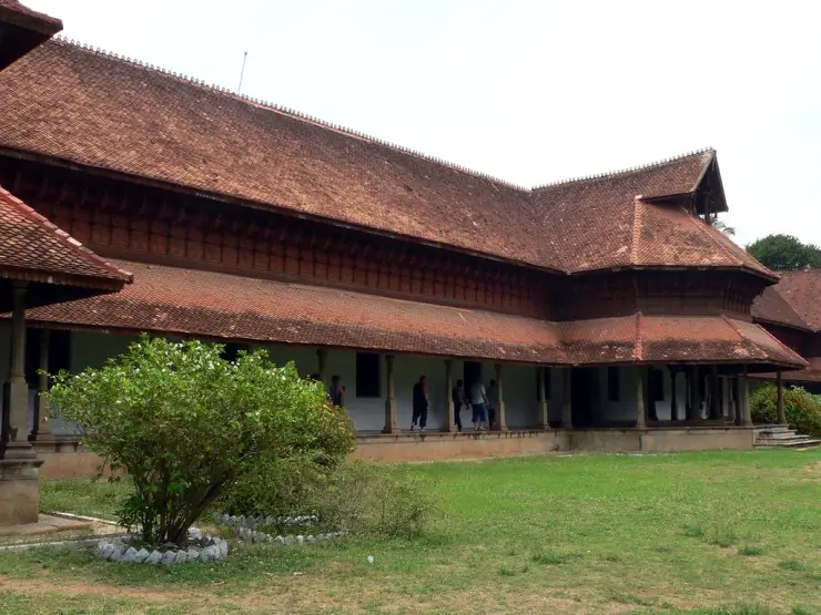 The pillared verandah of Kuthiramalika palace with visitors walking along it, seen across the lawn under the deep tiled roof
