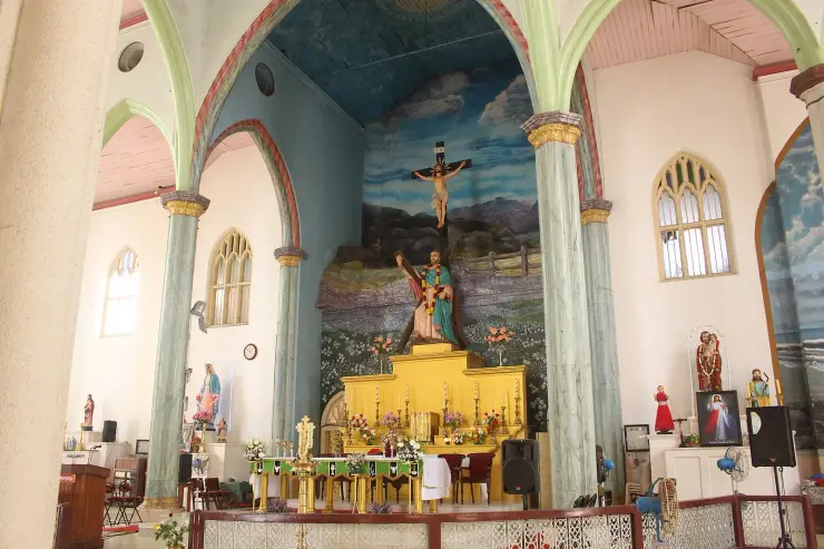 The sanctuary of St Andrew’s Basilica, Arthunkal, with a garlanded statue of St Andrew embracing his saltire cross before a painted landscape backdrop and a gold altar