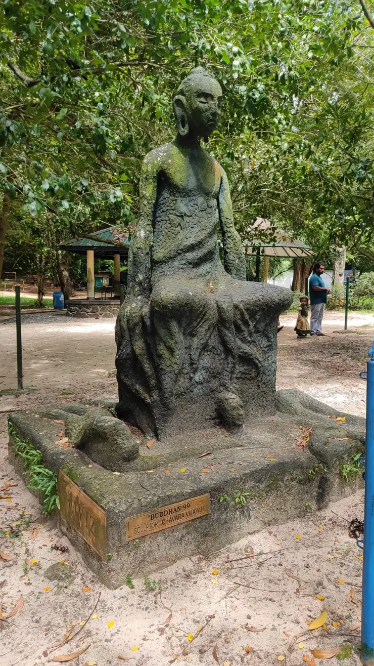 A contemporary sculpture titled Buddha 99 standing on open ground among trees in the Asramam park at Kollam