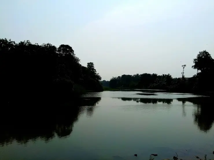 The Kallada river at Puthoor in flat grey light, a broad still reach reflecting dark tree-lined banks, with low hills on the horizon.