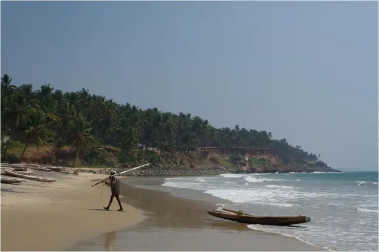 A fisherman working alone on the shore at Paravur, small country craft and nets on the sand.