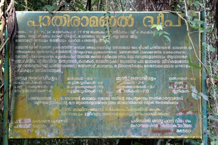 A weathered green government information board on Pathiramanal island, lettered in Malayalam with biodiversity counts