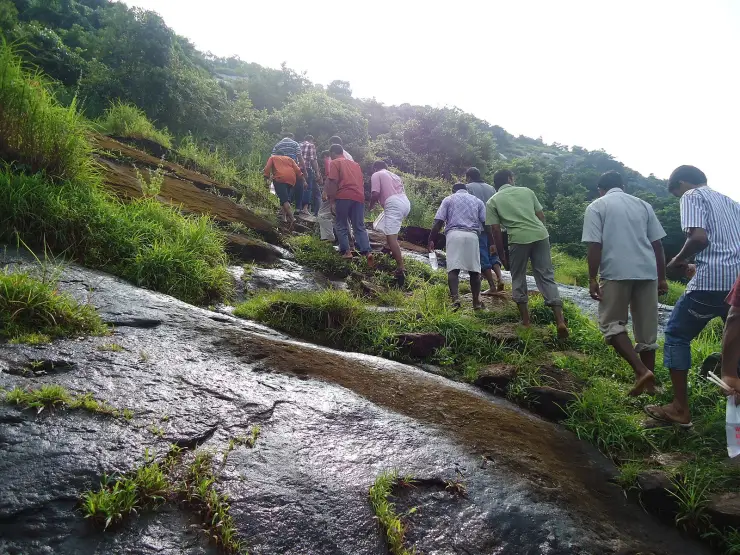 Pilgrims climbing a wet, bare rock slope on Kanakamala hill, most of them barefoot
