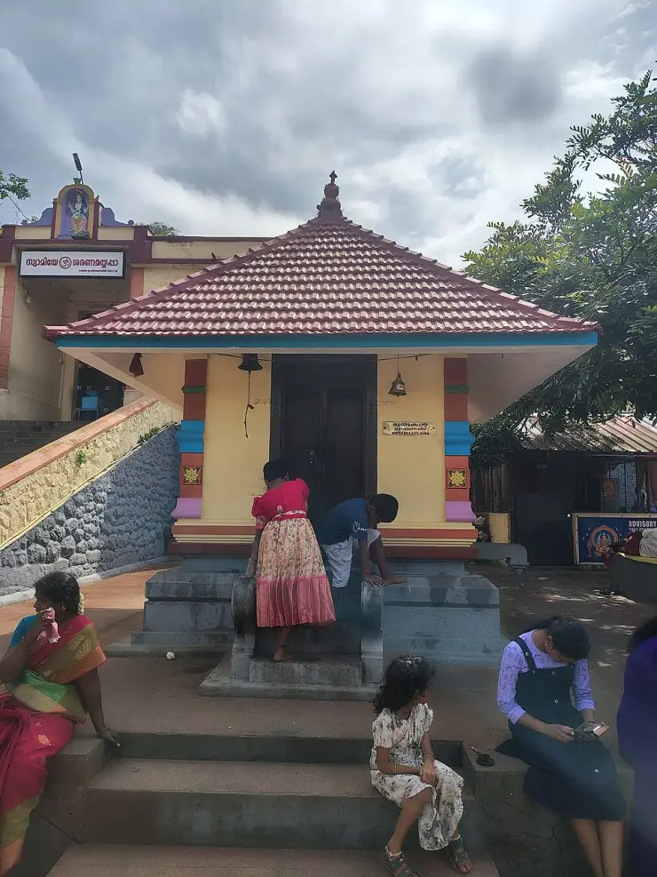 A small tiled sub-shrine signed Murugan, with several women and girls of different ages standing and sitting on the steps in front of it